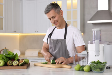 Poster - Juicer and fresh products on white marble table. Smiling man cutting cucumber in kitchen