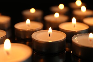 Many burning tealight candles on black background, closeup