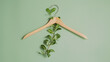 © Generative AI - Wooden clothes hanger with green leaves over light green background with copy space as a symbol of slow fashion and environmentally friendly fashion Reuse recycling and upcycling cloth : Generative AI