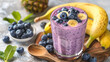 © reddish - A close-up of a refreshing blueberry banana smoothie topped with blueberries and banana slices. The smoothie is in a glass and sitting on a wooden board with fresh fruit around it