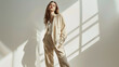 © Generative AI - Full length shot of a beautiful brownhaired girl fashion model posing in a loose beige pantsuit on a white studio background Elegant style Fashion shot : Generative AI