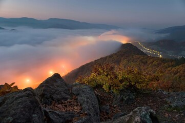 Poster - Autumn landscape with rocks, colorful leaves on the trees, inversion, city ​​lights in the fog . Awesome Autumn landscape.