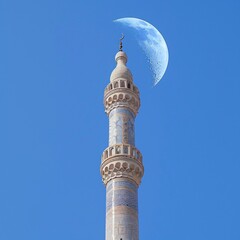 front view, Very tall mosque minaret, blue sky background, a curved moon in the sky