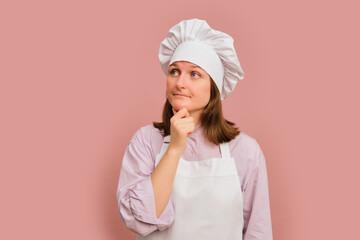 Pensive woman cook on studio pink background. Portrait of a female person in chef's clothing
