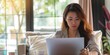 © Iryna - A young Asian woman working on her laptop at home, combining business and comfort.
