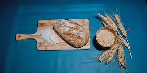 A loaf of bread sits on a wooden cutting board next to a bowl of flour