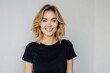 © pham - A young woman with blonde hair smiles at the camera in a simple black t-shirt against a white wall background