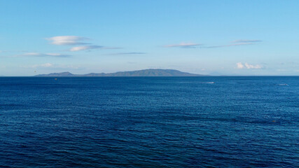 Wall Mural - The surface of a calm ocean. View of a calm sea, clouds in the sky and a tropical island on the horizon.