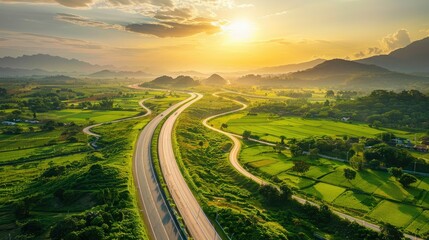 Wall Mural - Panorama aerial view of highway overpass curving through lush green landscape at sunset