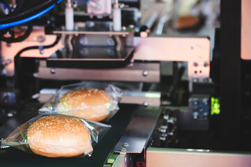 Poster - A machine is making hot dogs in plastic bags. The bags are being placed on a conveyor belt