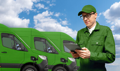 Poster - A man with a digital tablet stands next to green electric delivery vans