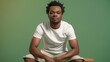 © Sabir Shah - Full Body Shot of Stylish African American Man in White T-Shirt Sitting on Stool, Smiling Confidently Against Lush Green Background with Sophisticated Muted-Green Color Scheme and Volumetric Lighting