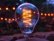 © Nataliya - Lightbulb with bright filament glowing in a dark outdoor setting