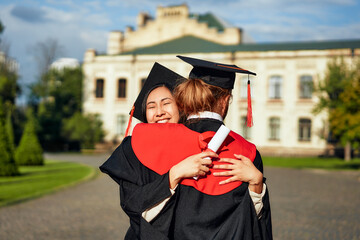 Wall Mural - A scene of celebration Two students embracing while wearing graduation cap and gown