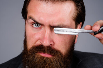 Wall Mural - Barbershop. Closeup portrait of bearded man with straight razor. Professional beard care. Handsome bearded man with razor. Salon for men. Barber shop service. Hairdresser with barbershop equipment.