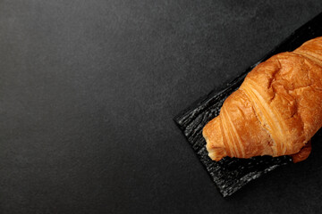 Wall Mural - Crispy hot croissant on a black rectangular wooden board on a gray background