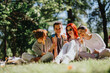 © qunica.com - A group of young friends sitting on grass in a park, enjoying colorful lollipops on a sunny day, radiating happiness and joy.