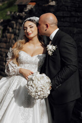 Wall Mural - A bride and groom are kissing each other's cheeks. The bride is wearing a white dress and the groom is wearing a black suit