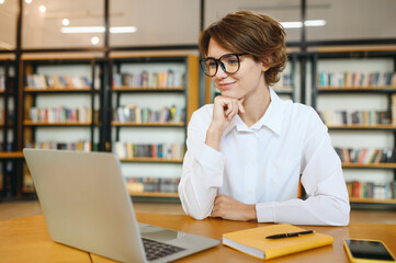 Wall Mural - Young smiling happy successful employee IT business woman wears white shirt casual clothes glasses hold use work on laptop pc computer surfing internet sit at office desk. Achievement career concept.