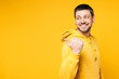 © ViDi Studio - Side view young smiling happy man wear hoody casual clothes point thumb finger aside on area mockup workspace look camera isolated on plain yellow orange background studio portrait. Lifestyle concept