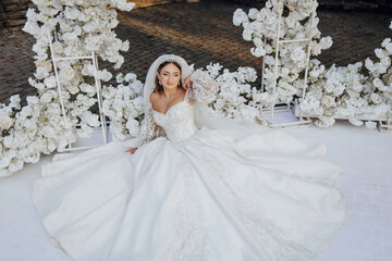 Wall Mural - A woman in a white wedding dress is sitting on a white carpet. She is wearing a veil and a white headband