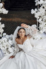 Wall Mural - A woman is sitting in a white dress with a veil on her head. She is wearing a wedding dress and is surrounded by white flowers