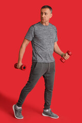 Poster - Portrait of sporty middle-aged man exercising with dumbbells on red background