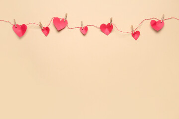 Red paper hearts hanging on rope against color background