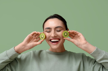 Wall Mural - Happy young woman with tasty kiwi on green background