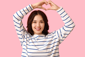 Wall Mural - Pretty young Asian woman showing heart gesture on pink background. Valentine's Day celebration