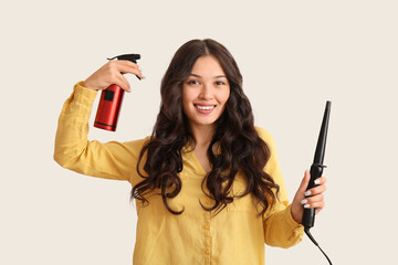 Sticker - Young Asian woman with curling iron and hair spray on light background