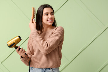 Canvas Print - Beautiful young happy woman with brush and hair dryer on green background