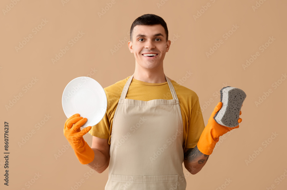 Young tattooed man with plate and sponge on beige background