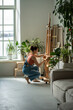 © DimaBerlin - Creative female artist adjusting height of easel before starting work. Focused woman preparing workplace workspace for oil painting process on canvas. Girl painter in sunny apartment home art studio.