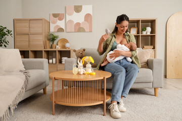 Wall Mural - Mother with toy breastfeeding her baby on sofa at home