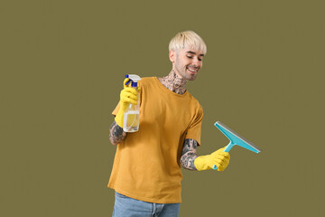 Poster - Young tattooed man with bottle of detergent and squeegee on green background