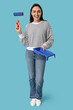 © Pixel-Shot - Young woman with paint roller and tray on blue background