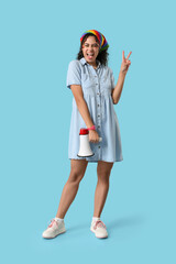 Sticker - Happy African-American woman with rainbow headscarf and megaphone showing victory gesture on blue background. LGBT concept