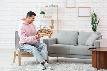 Poster - Young man holding cardboard box with tasty pizza at home