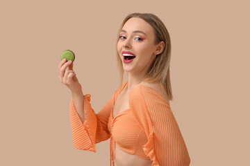 Wall Mural - Happy young woman with green sweet macaroon on beige background