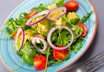 Wall Mural - Healthy arugula salad with avocado, cherry tomatoes and onion served on colored ceramic plate