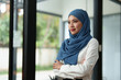 © crizzystudio - Modern office Muslim businesswoman wearing a hijab stands smiling confidently working on a financial project. Do analysis, calculations, startup business ideas, e-commerce, online.