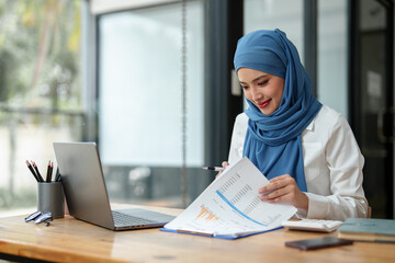 Wall Mural - Modern office Muslim businesswoman wearing hijab sits with laptop online, doing paperwork Sitting and working on financial projects, analysis, calculations, startup business ideas, e-commerce, online.