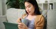 © Johnstocker - Portrait of Young asian woman drinking coffee while sitting relaxing on the sofa and playing social media on digital tablet in the living room at morning ,Free time