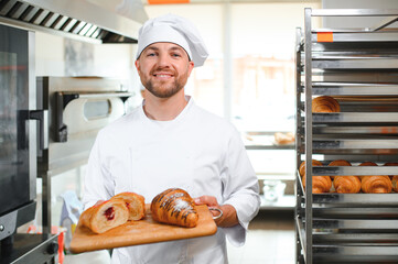 Smiling baker holding tray with fresh cooked croissants in bakehouse