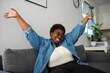 © Westend61 - Cheerful young woman with arms raised sitting on sofa in living room at home