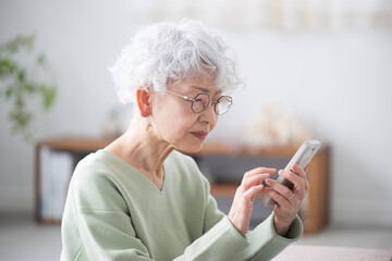 Wall Mural - smiling senior woman with a smart phone (smartphone) presbyopia makes it difficult to see the phone