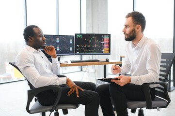 Two men colleagues traders sitting at desk at office monitoring stock market