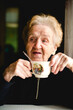 © De Visu - An elderly woman enjoys a cup of tea, savoring a peaceful and comforting moment.