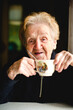 © De Visu - An elderly woman sips tea from a cup, capturing a serene moment of relaxation and comfort.